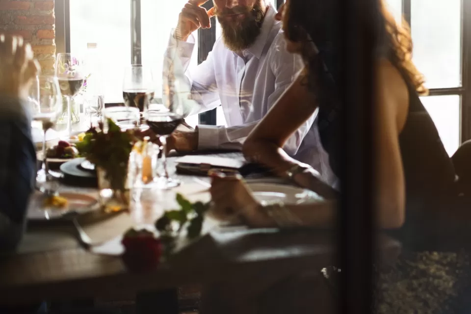 Blurry close-up of people eating at restaurant table with white wine glass in middle